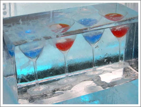 vier Cocktailgläser mit blauem und rotem Inhalt im Eisblock