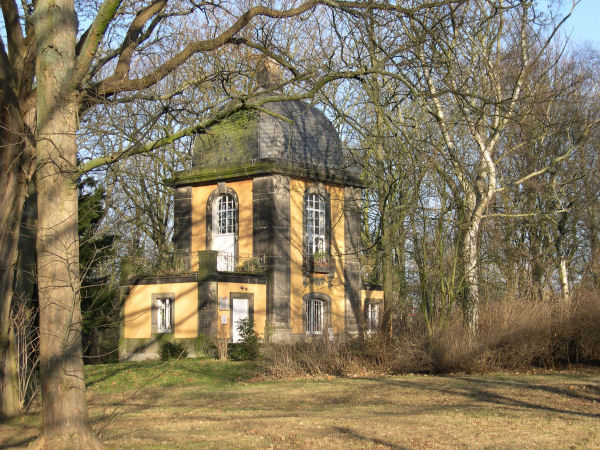 Foto: Haus mit orangefarbener Fassade und Kuppeldach zwischen Bumen
